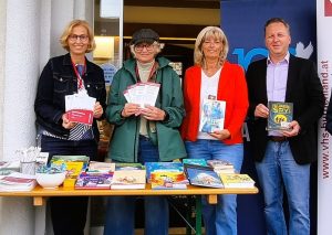 Vier Personen, die vor einem Büchertisch stehen und Bücher und Broschüren hochhalten.