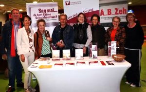 Gruppe hinter einem Tisch mit Flyern und vor Rollups der Burgenländischen Volkshochschulen. Alle blicken in die Kamera und lächeln.
